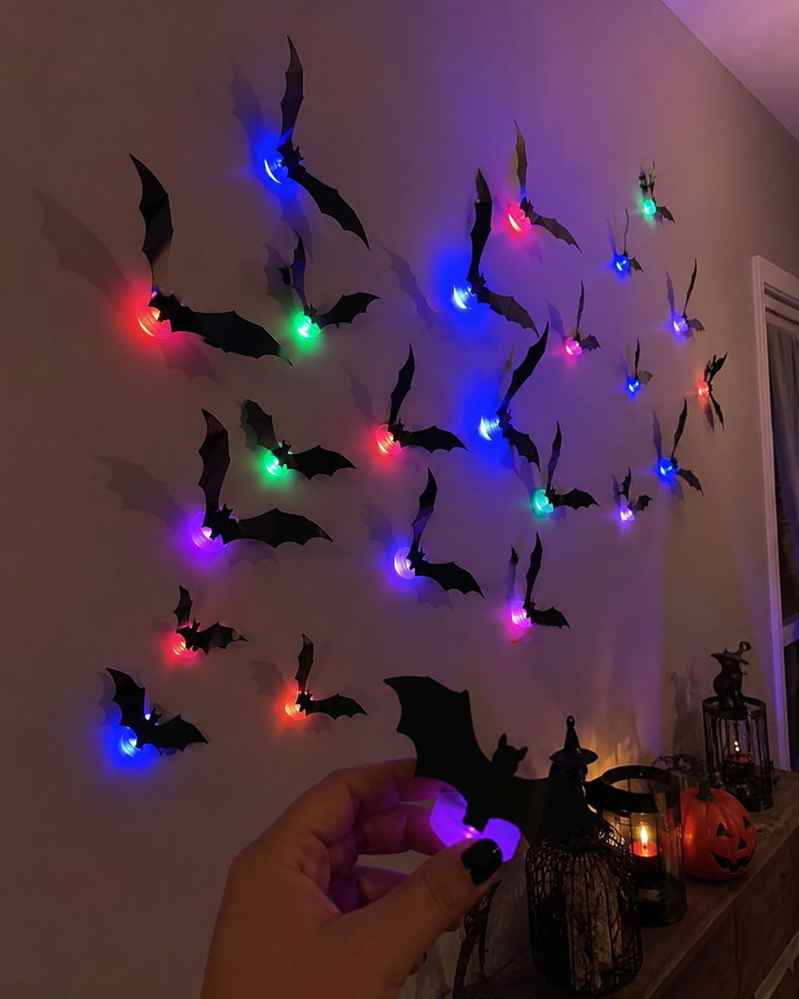Colorful illuminated bat decorations displayed on a covered porch wall